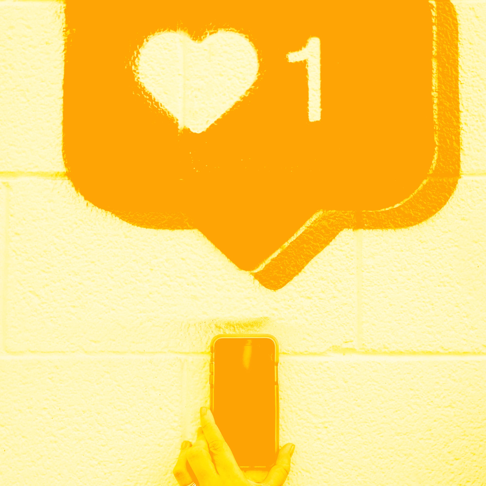 hand holding phone under instagram heart like notification brick wall golden