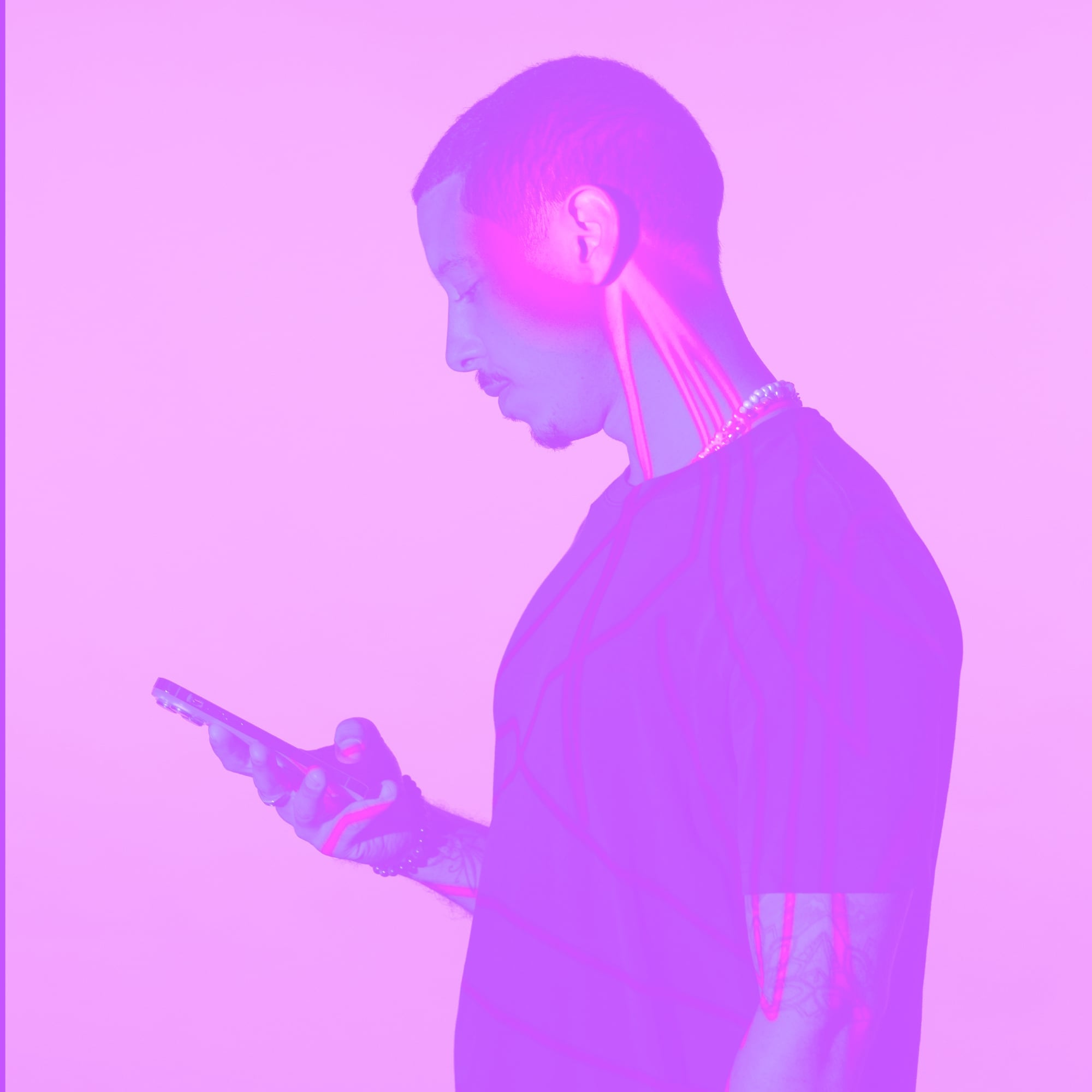 man with braids looking at smartphone side profile pink purple toned