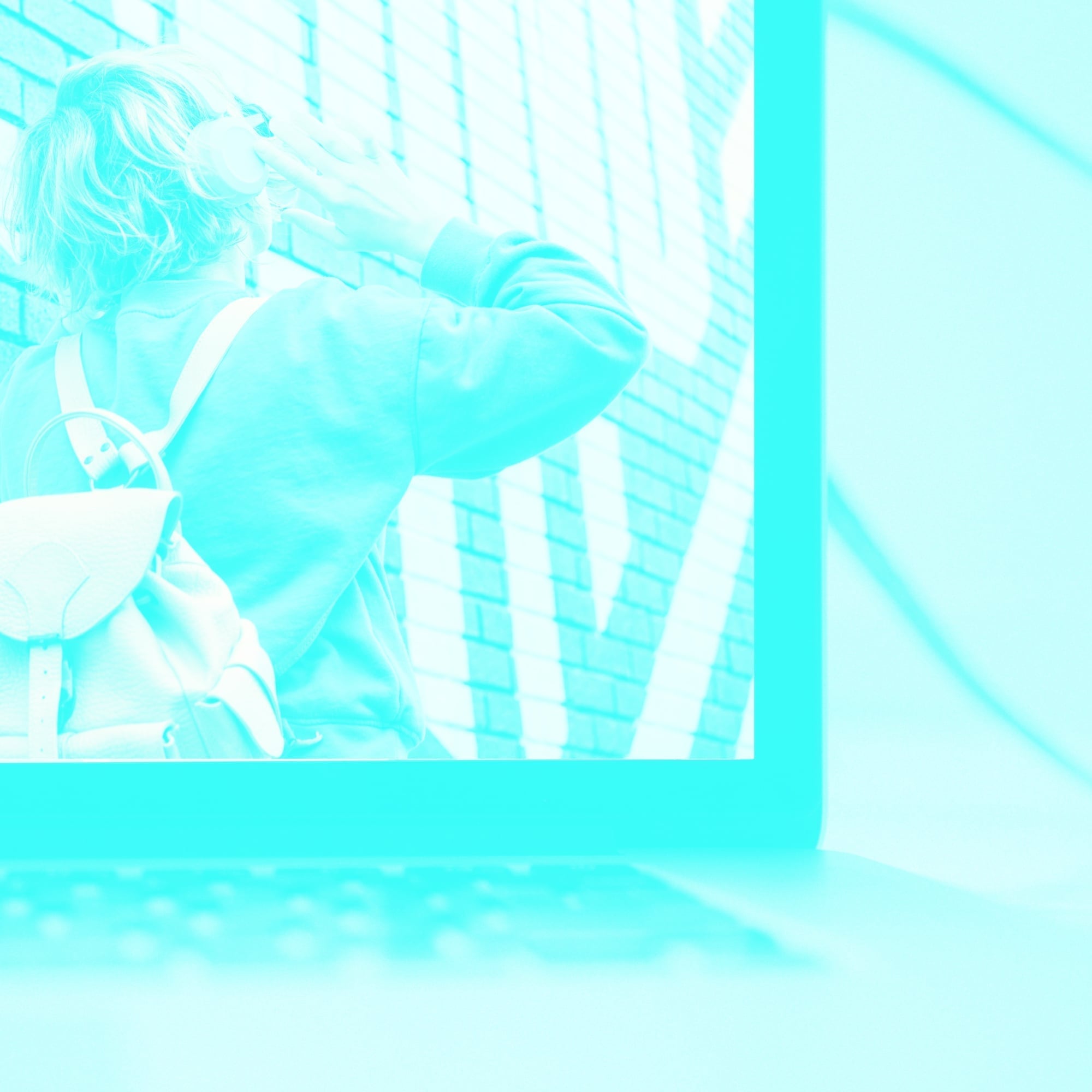 laptop screen showing woman with bag next to brick wall teal toned
