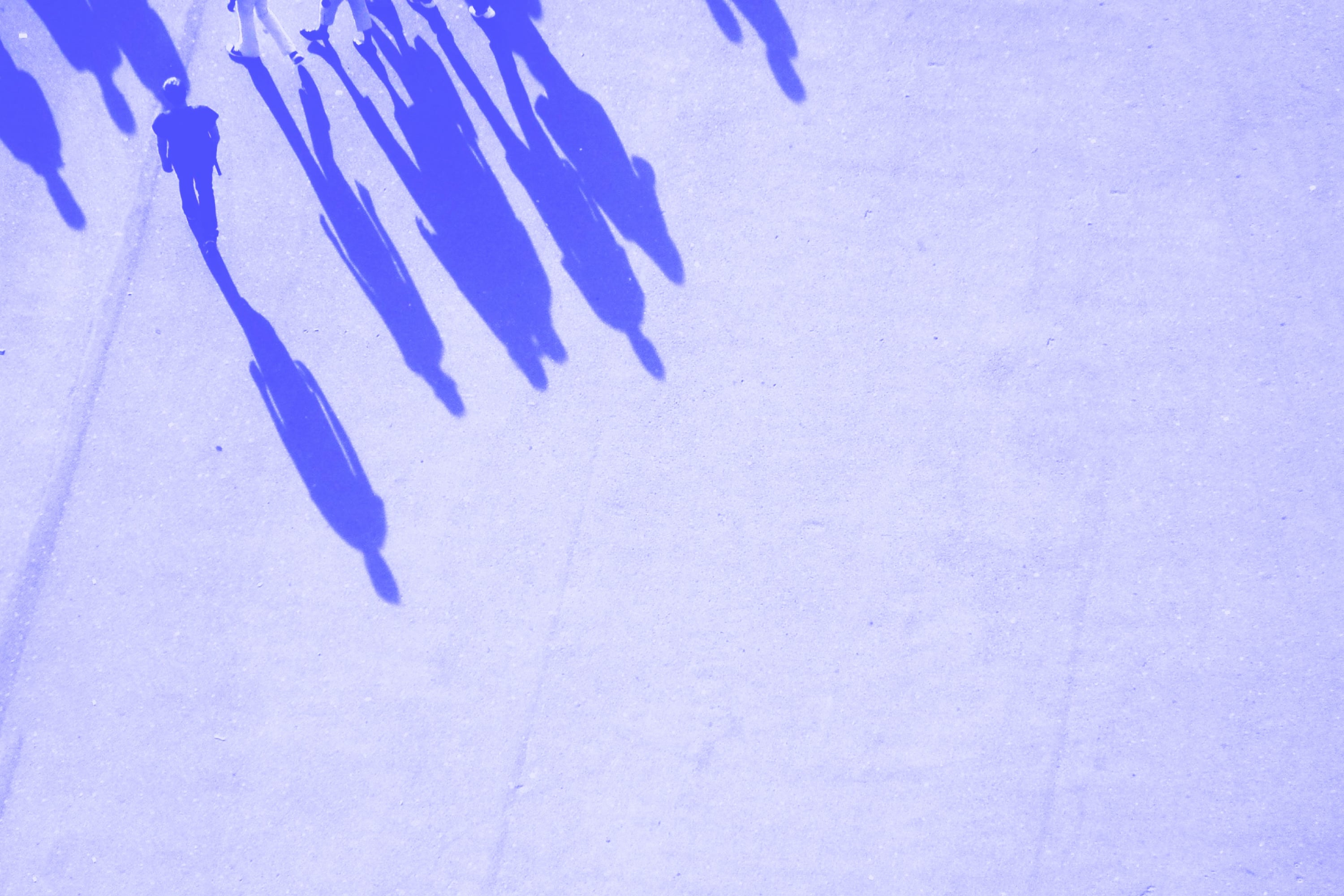 aerial view of people walking with shadows on concrete pavement blue toned
