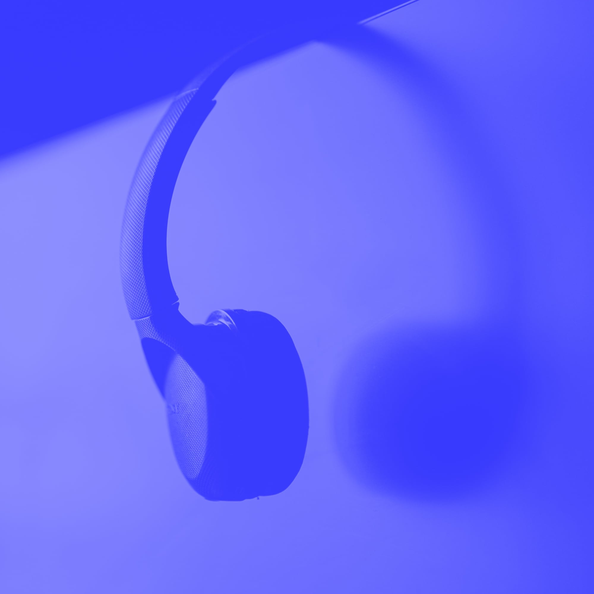 wireless over ear headphones hanging on monitor corner blue toned
