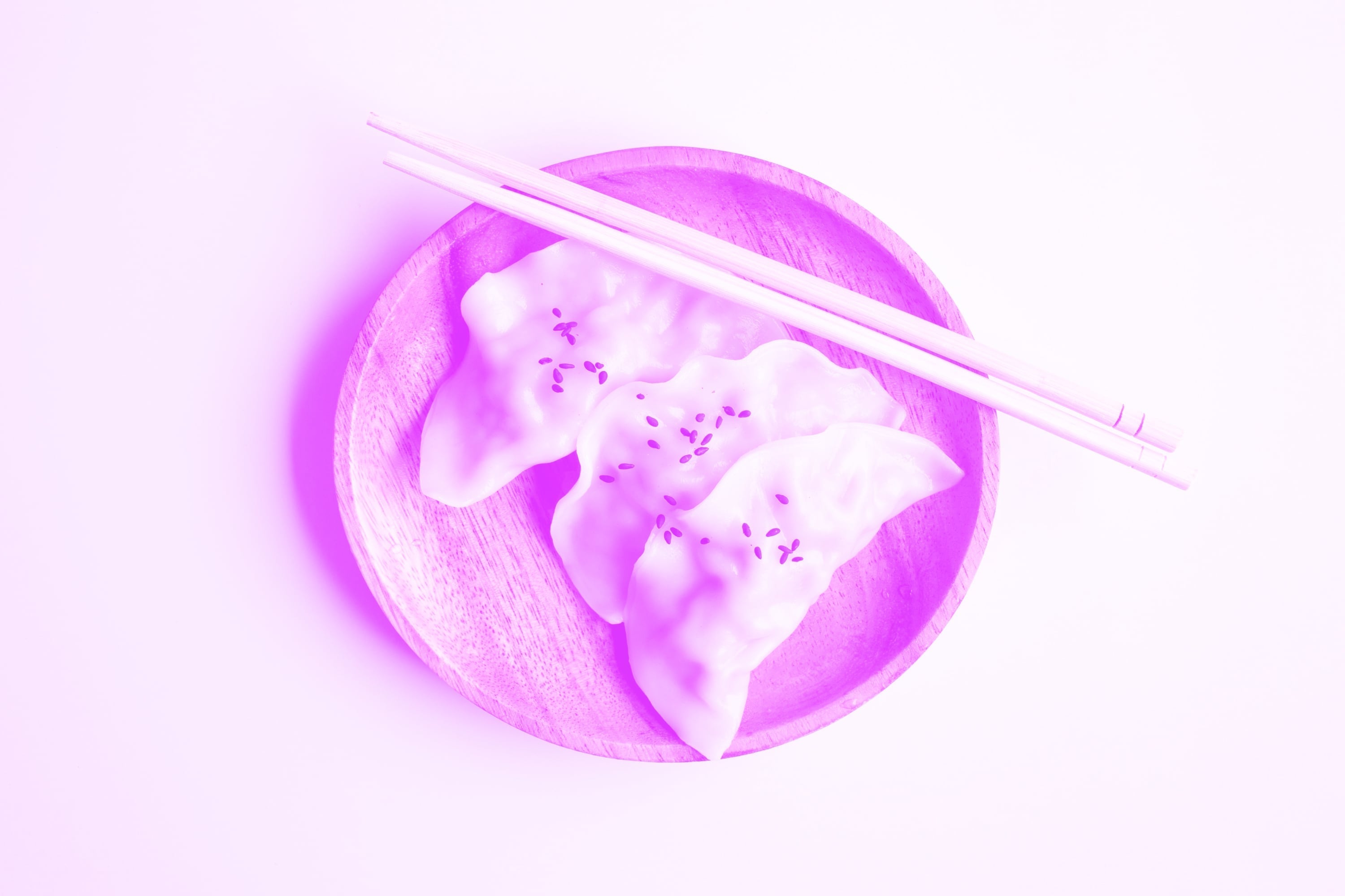 three gyoza dumplings with sesame seeds on wooden board with chopsticks pink purple