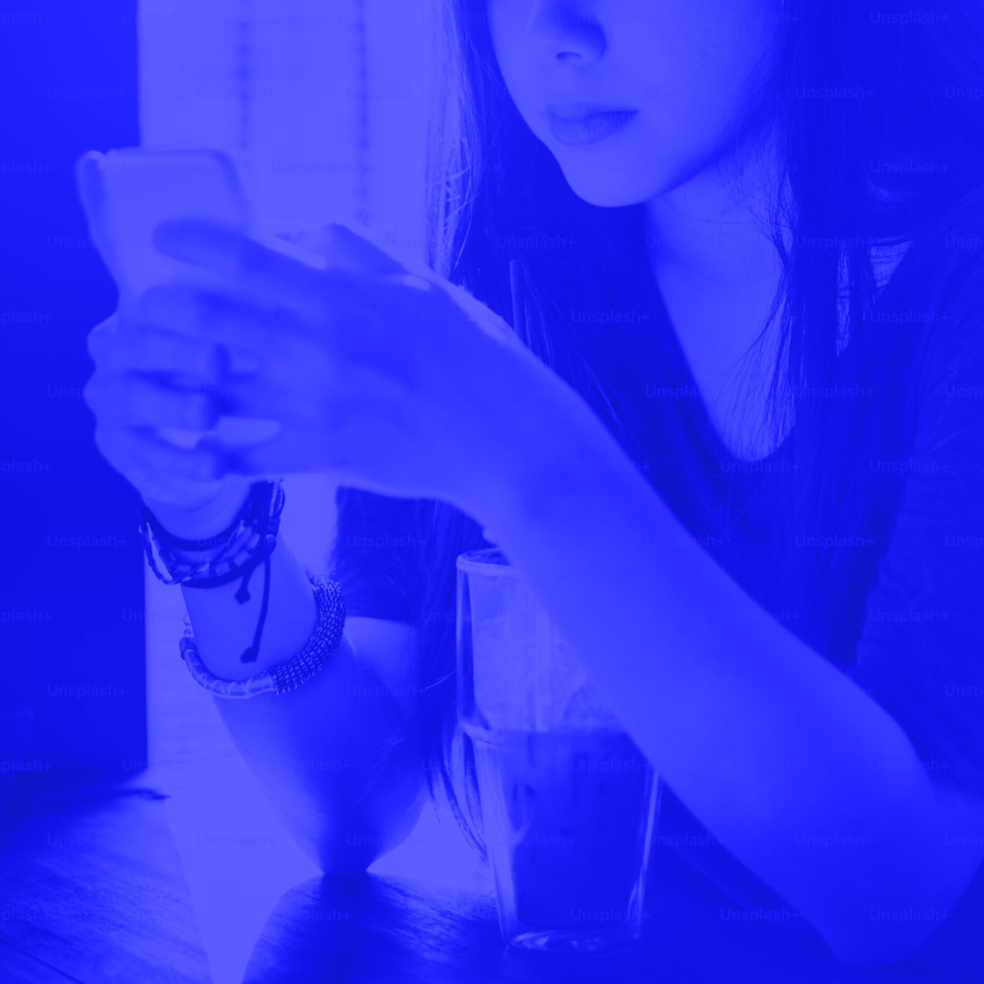 young woman with long hair holding smartphone and coffee cup blue toned