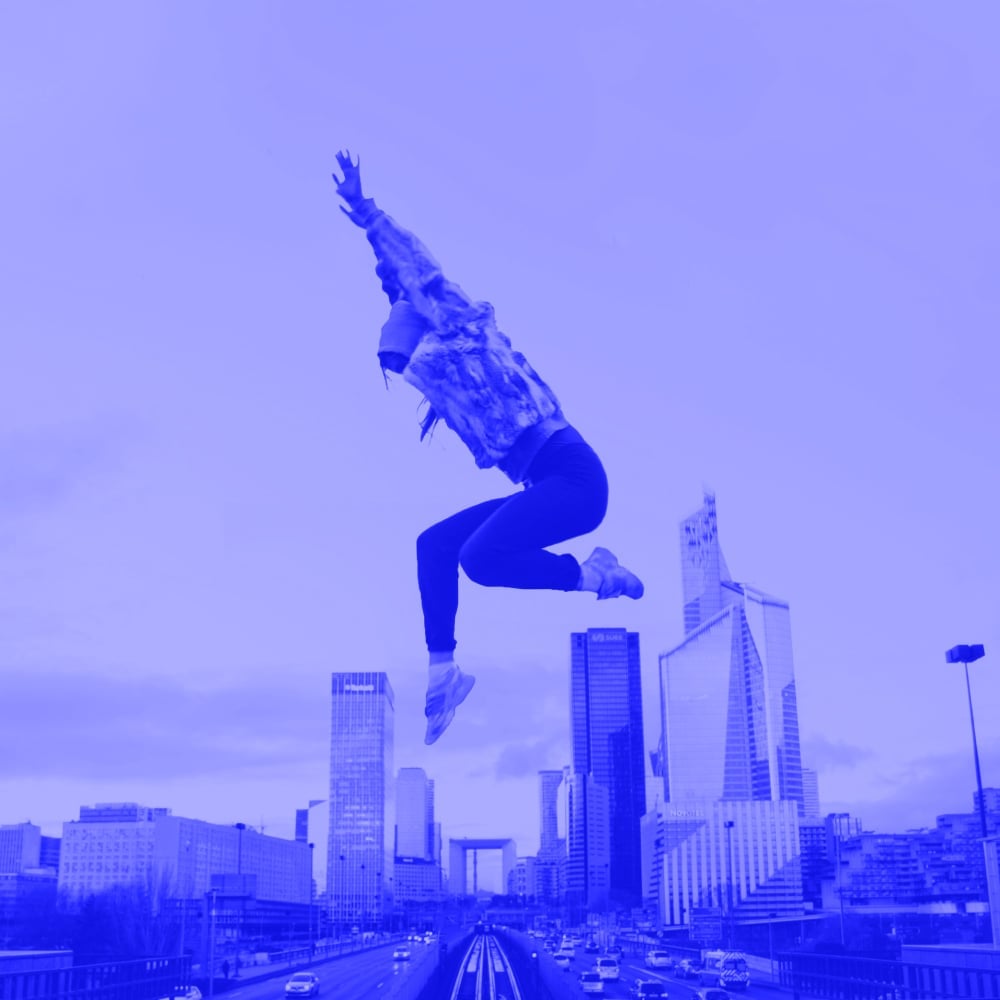 woman jumping high above city skyline with arms raised blue toned