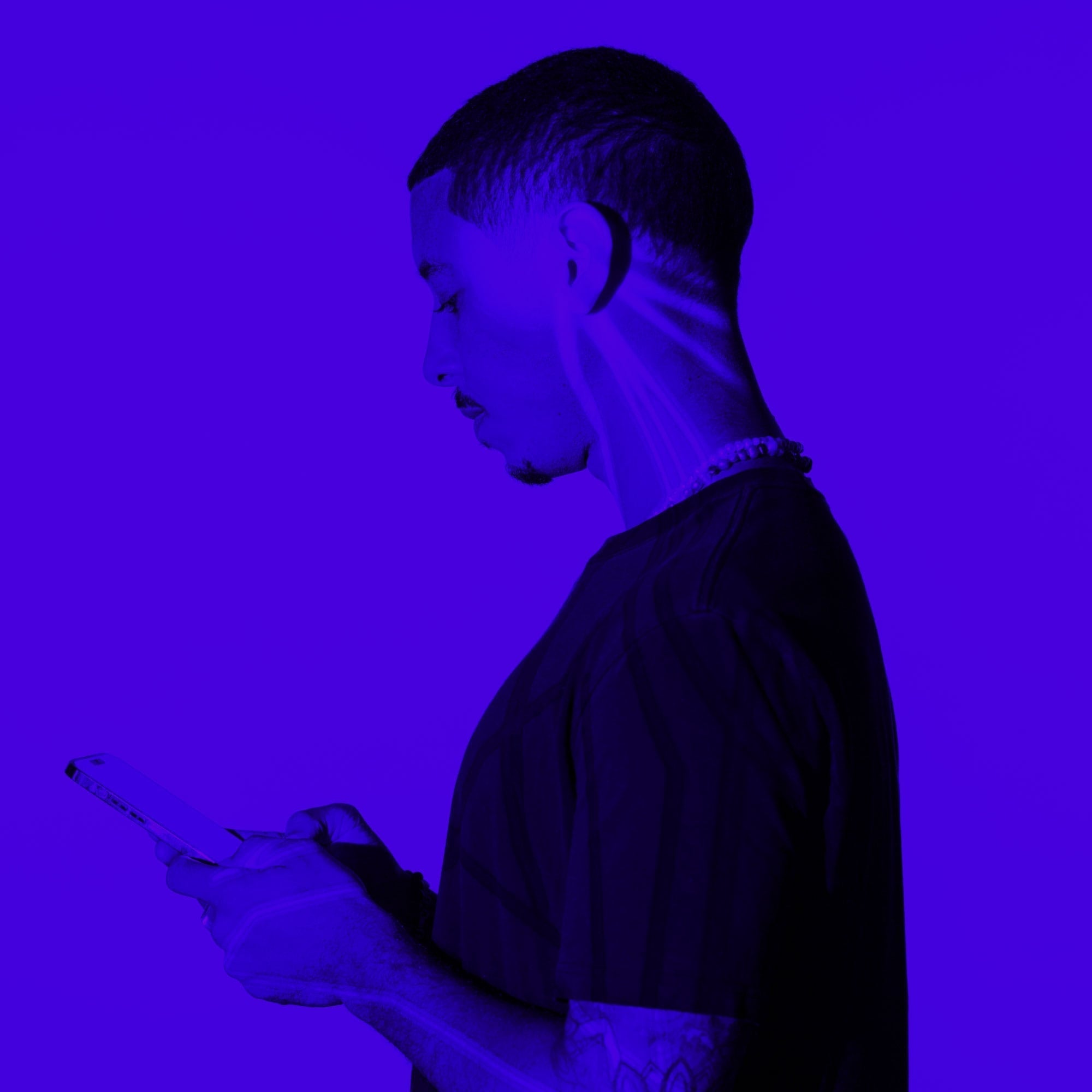 man with shaved head browsing smartphone side profile purple toned