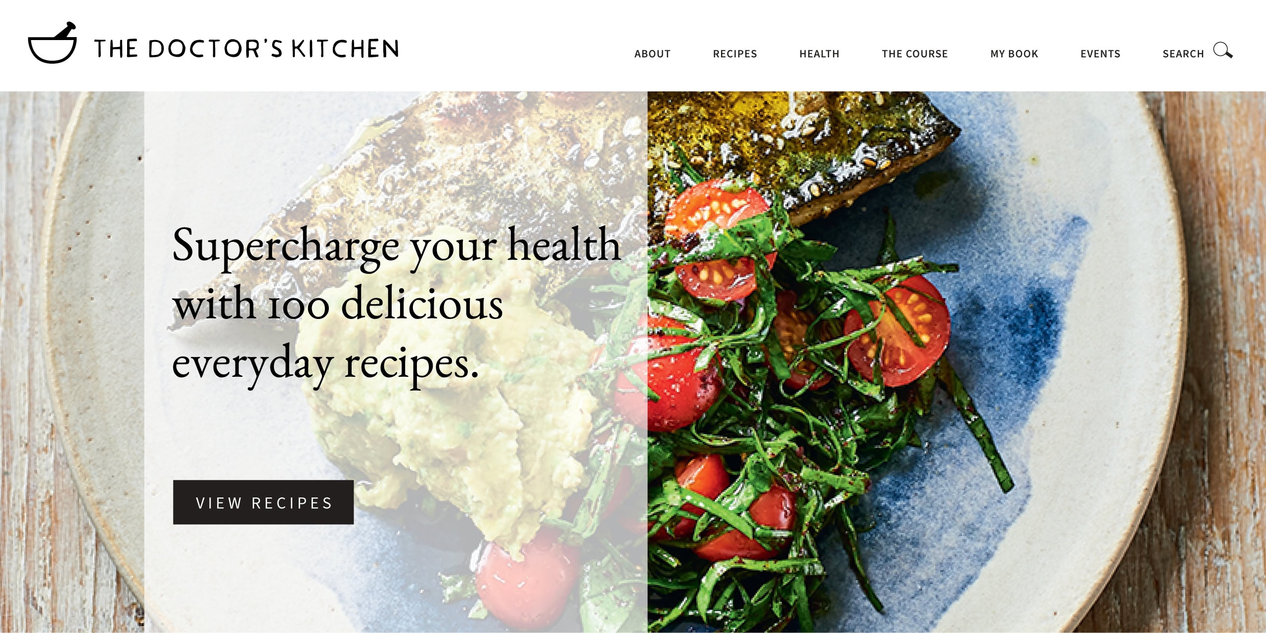 Hero section from The Doctor's Kitchen website with a beautiful overhead shot of grilled fish and vine tomatoes with branding, navigation and the strapline 'Supercharge your health with 100 delicious everyday recipes.