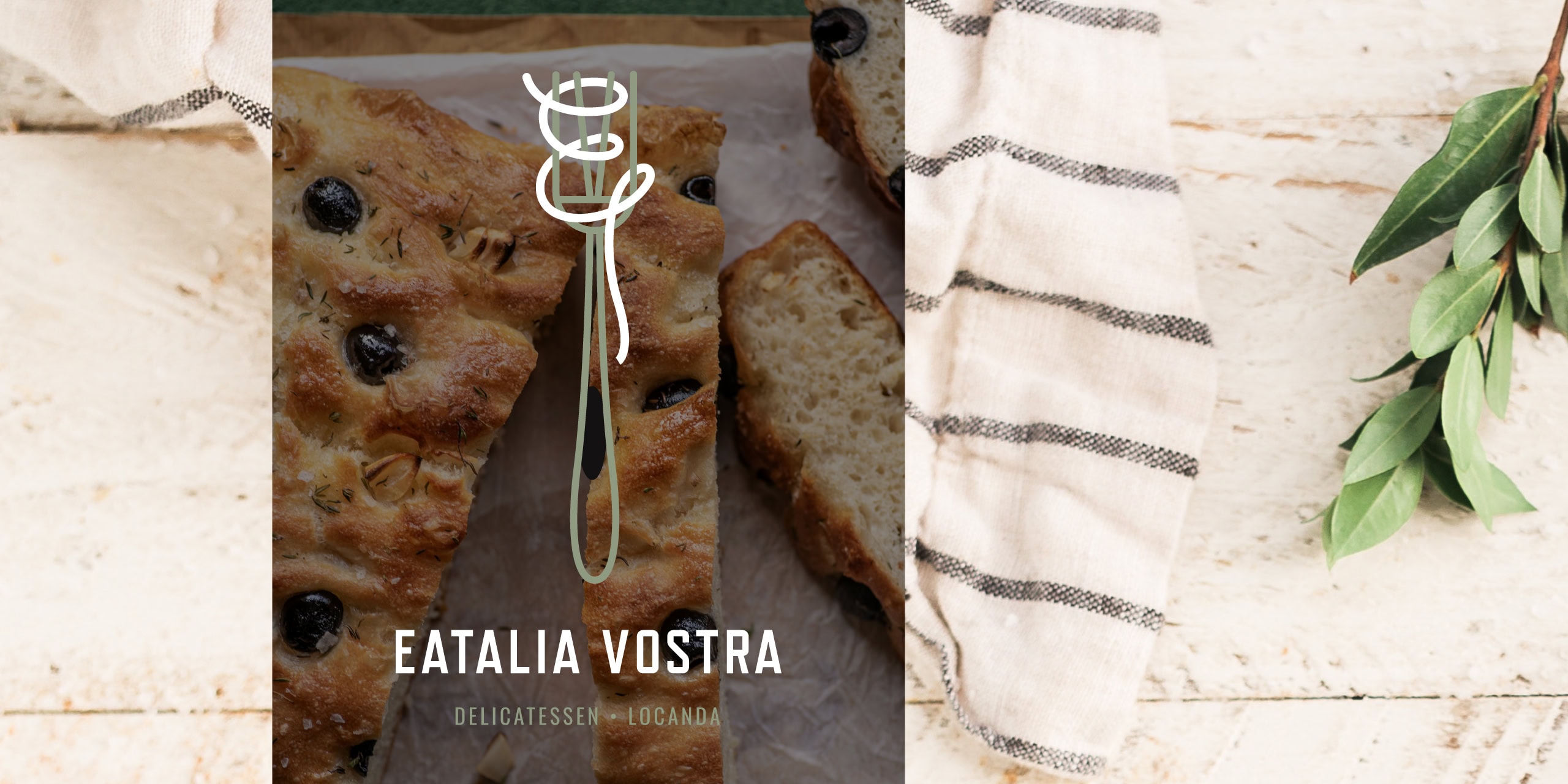 Eatalia Vostra lockup over olive focaccia with linen cloth and olive branch on a rustic tabletop