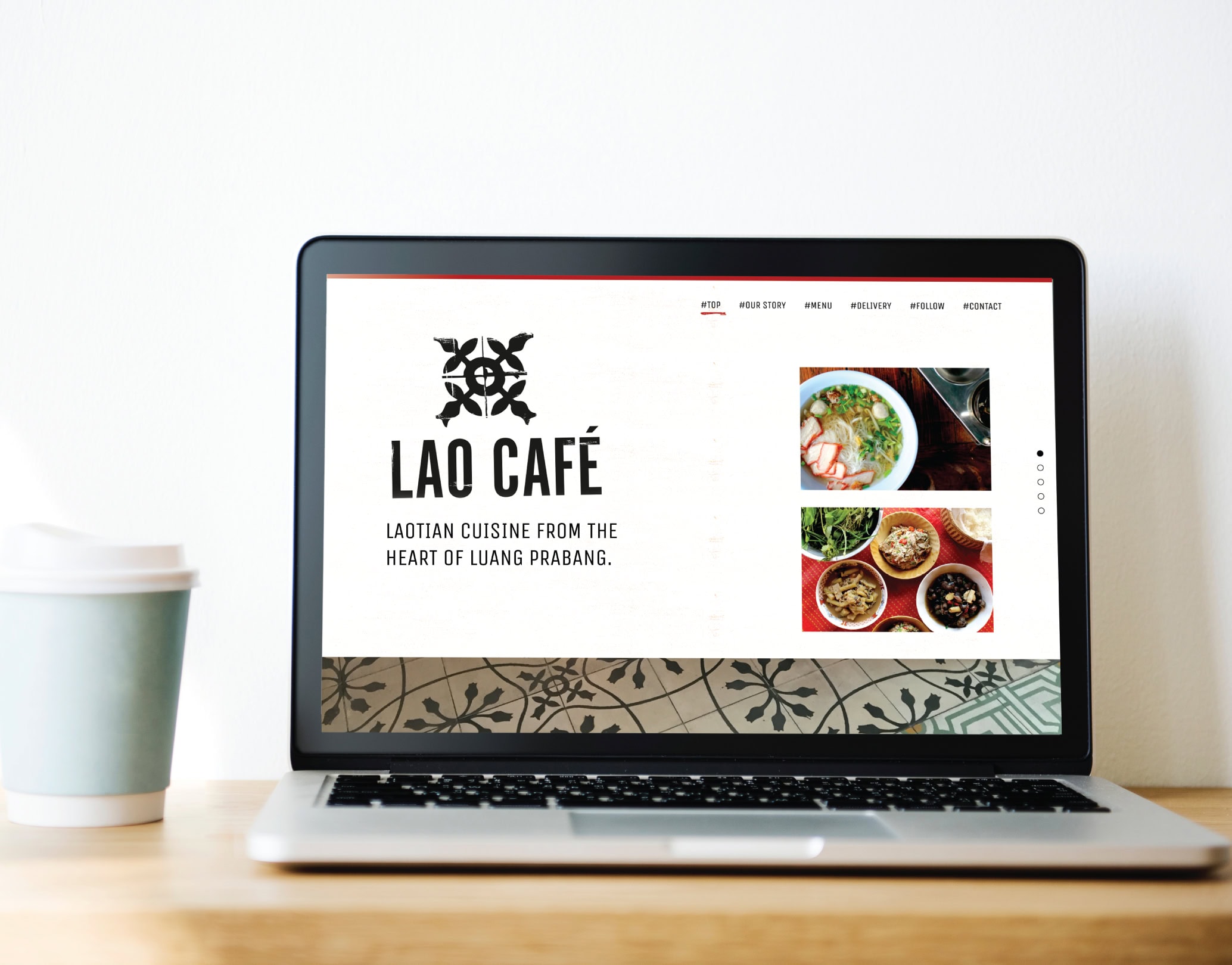 Laptop on a desk showing the Lao Café one-page website layout, with food photography panels and a takeaway coffee beside it