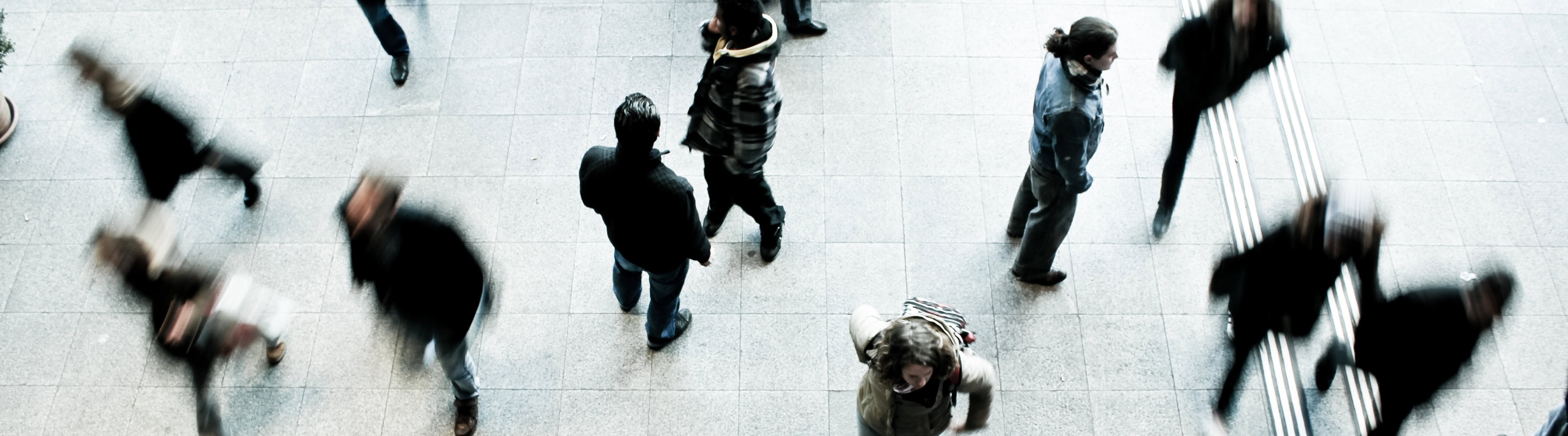 Overhead view of people walking across a tiled floor, with motion blur showing a busy public space