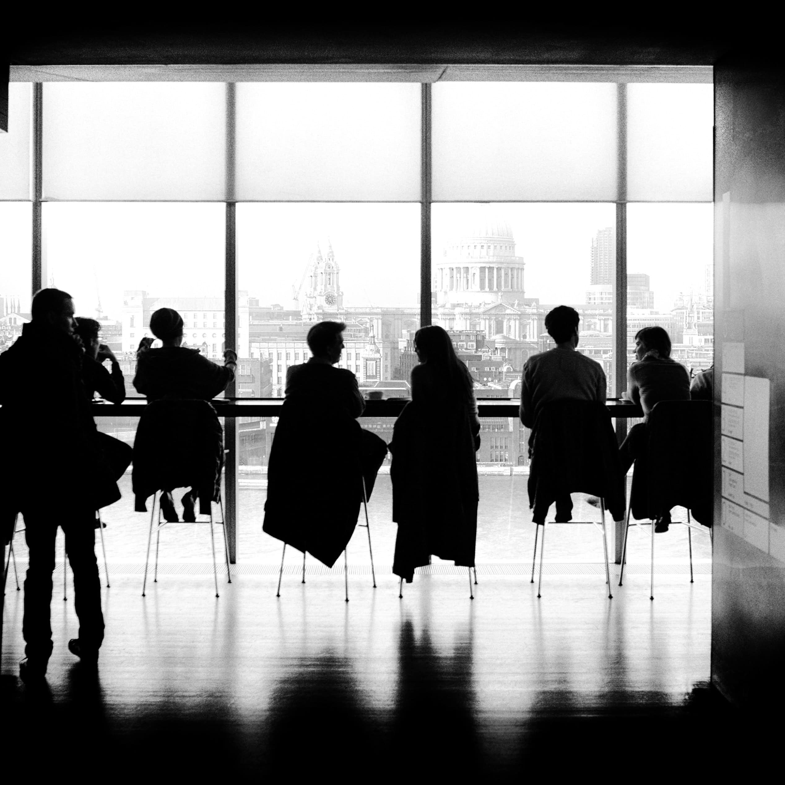Silhouettes of people seated by a large window overlooking the London skyline