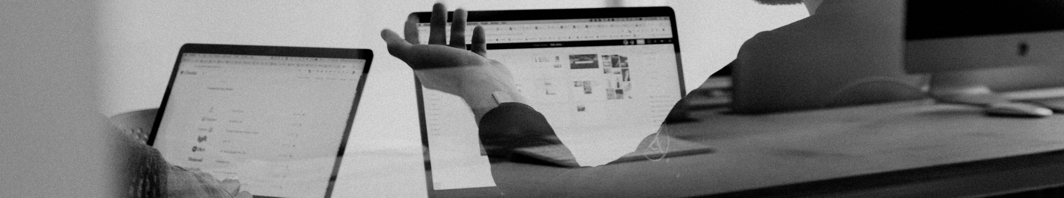 Two people in discussion in front of laptop computers at a desk.