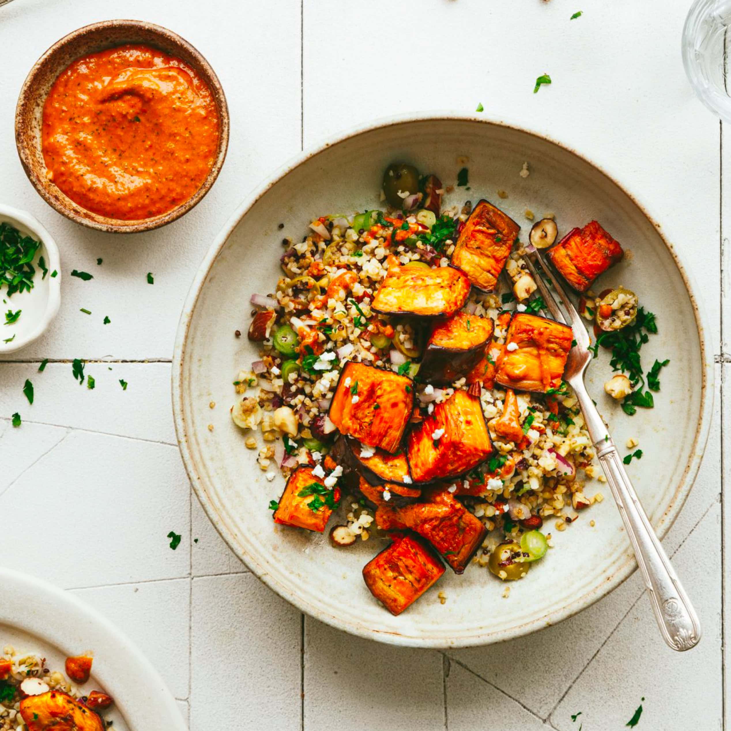 Overhead photo of a grain bowl topped with roasted aubergine and herbs